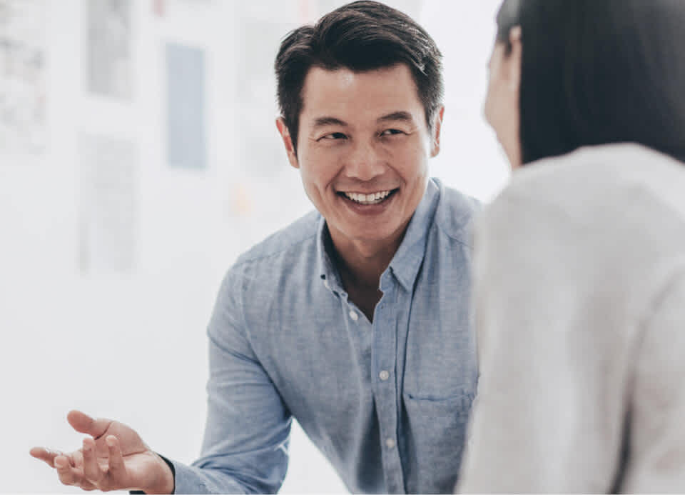 A man in a chambray shirt shows someone something in a meeting