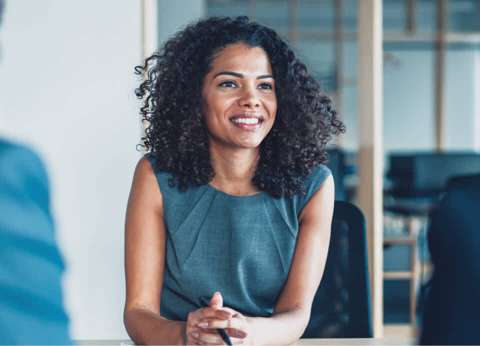 A woman in a teal dress sits in a meeting