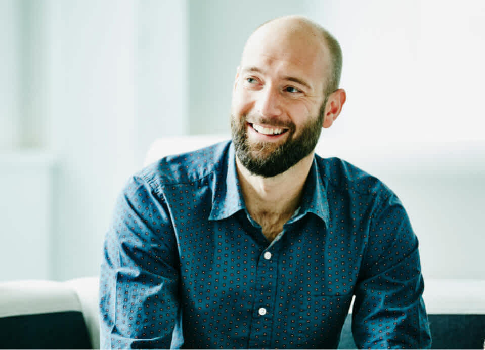 A man in a teal shirt smiles during a meeting